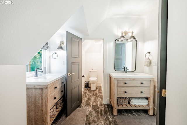 bathroom with two vanities, vaulted ceiling, toilet, and wood finished floors