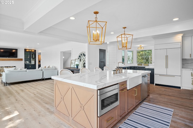 kitchen featuring built in appliances, a sink, light wood-style floors, a kitchen island with sink, and light stone counters