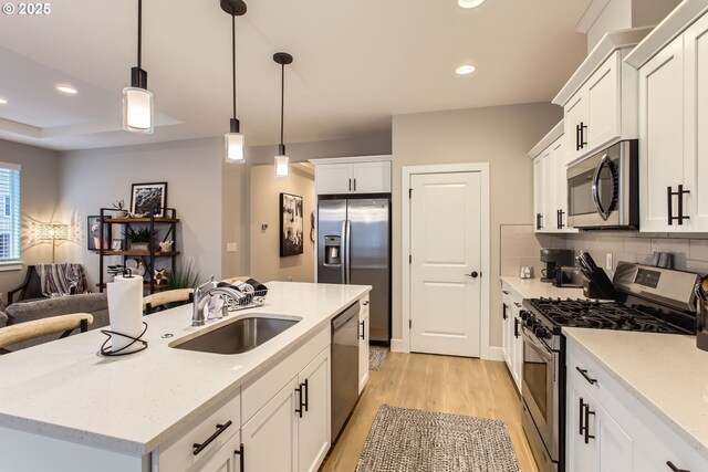 kitchen featuring sink, appliances with stainless steel finishes, white cabinets, a center island with sink, and decorative light fixtures