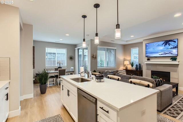 kitchen featuring sink, dishwasher, white cabinetry, hanging light fixtures, and a center island with sink