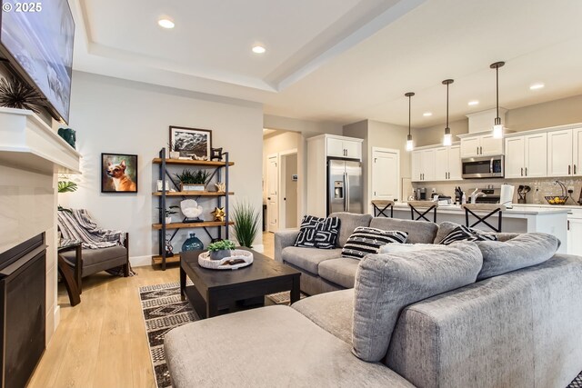 living room with a tiled fireplace, light hardwood / wood-style floors, and a tray ceiling