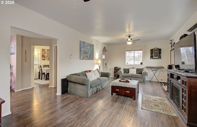 living room featuring a healthy amount of sunlight, dark wood-type flooring, an AC wall unit, and ceiling fan