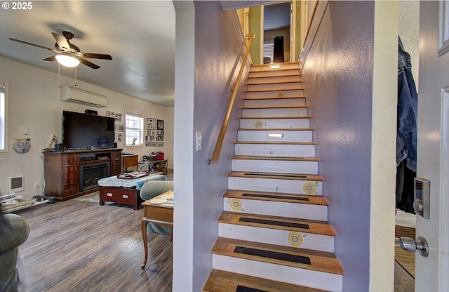 stairway featuring wood-type flooring, an AC wall unit, and ceiling fan