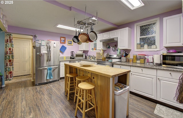 kitchen with butcher block counters, appliances with stainless steel finishes, a kitchen breakfast bar, a kitchen island, and white cabinets