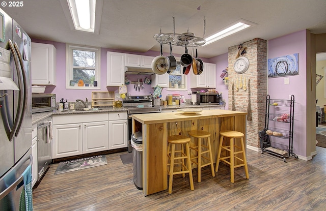 kitchen with white cabinetry, wood counters, stainless steel appliances, and a center island