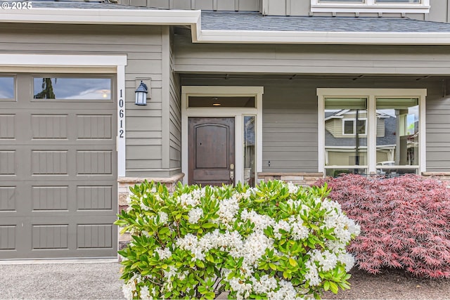 view of exterior entry with a garage, covered porch, stone siding, and roof with shingles