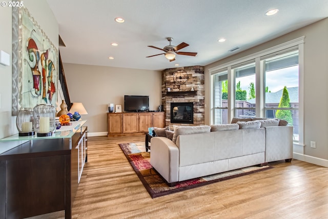living room featuring a ceiling fan, light wood finished floors, baseboards, recessed lighting, and a stone fireplace