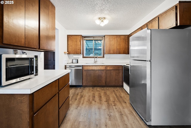 11613 Pacific Ct NE, Woodburn, OR 97071 - kitchen featuring stainless steel appliances, light countertops, light wood finished floors, a textured ceiling, and brown cabinets