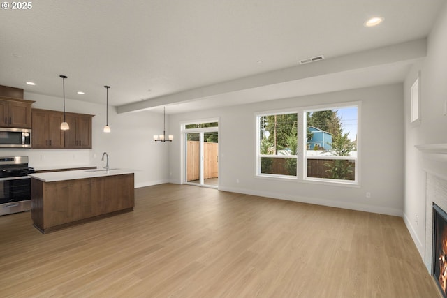 kitchen with sink, light hardwood / wood-style flooring, a kitchen island with sink, hanging light fixtures, and stainless steel appliances