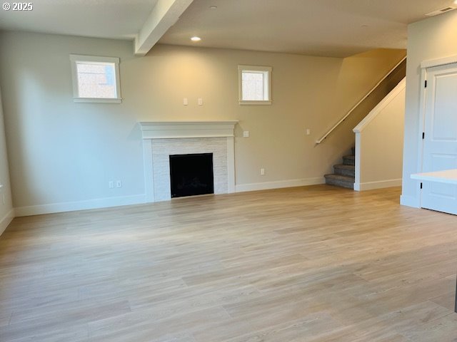 unfurnished living room with a wealth of natural light, beamed ceiling, and light wood-type flooring