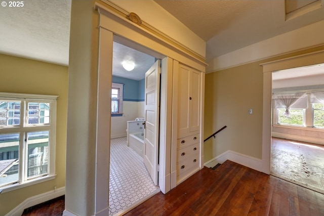 corridor with an upstairs landing, baseboards, a textured ceiling, and dark wood finished floors