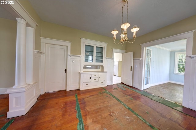 unfurnished dining area with ornate columns, a decorative wall, hardwood / wood-style floors, and a notable chandelier