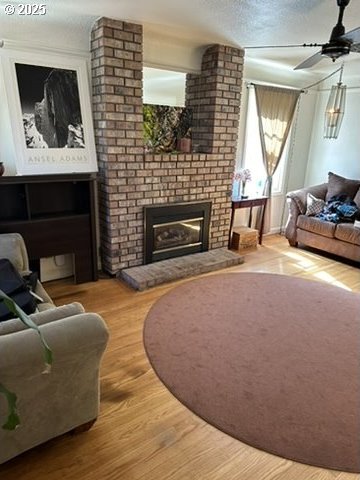 living room with a textured ceiling, a fireplace, a ceiling fan, and wood finished floors