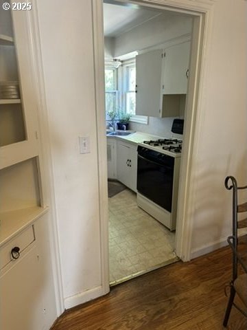 kitchen featuring white range with gas cooktop, white cabinets, light countertops, light wood-style floors, and a sink