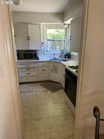 kitchen featuring a sink, white cabinetry, light floors, stainless steel microwave, and gas stove