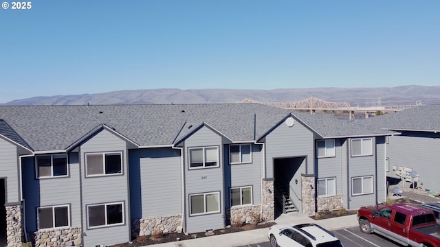 view of front of house with a shingled roof, uncovered parking, and a mountain view