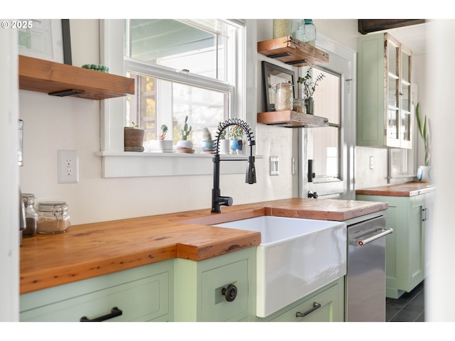 kitchen with butcher block countertops, dark tile patterned floors, a sink, dishwasher, and green cabinets