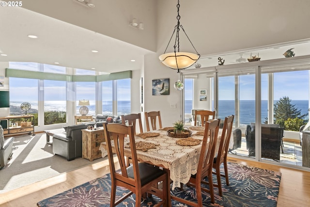 dining area featuring a water view, a towering ceiling, and light wood-type flooring