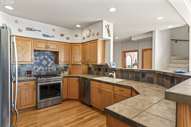 kitchen with sink, appliances with stainless steel finishes, light hardwood / wood-style floors, decorative backsplash, and tile countertops