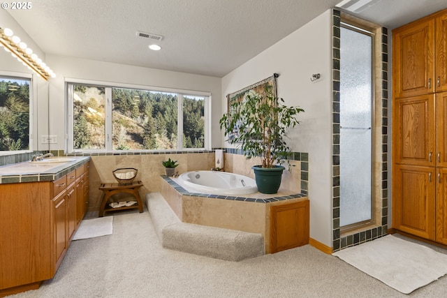 bathroom featuring vanity, a relaxing tiled tub, and a textured ceiling