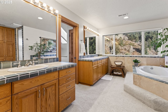 bathroom featuring vanity, tiled bath, and a textured ceiling