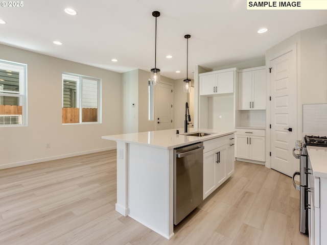 kitchen featuring light wood finished floors, appliances with stainless steel finishes, a sink, and white cabinets