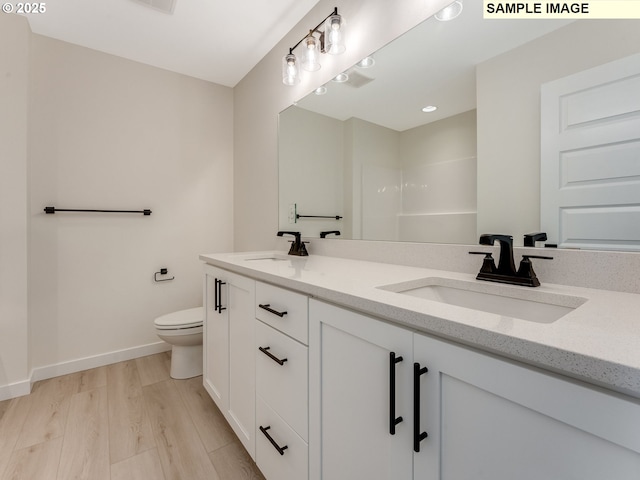 full bath featuring toilet, double vanity, a sink, and wood finished floors