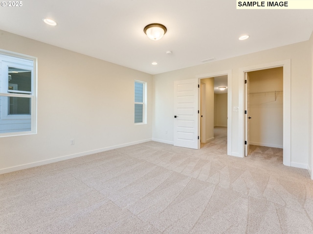 unfurnished bedroom with baseboards, a spacious closet, recessed lighting, and light colored carpet