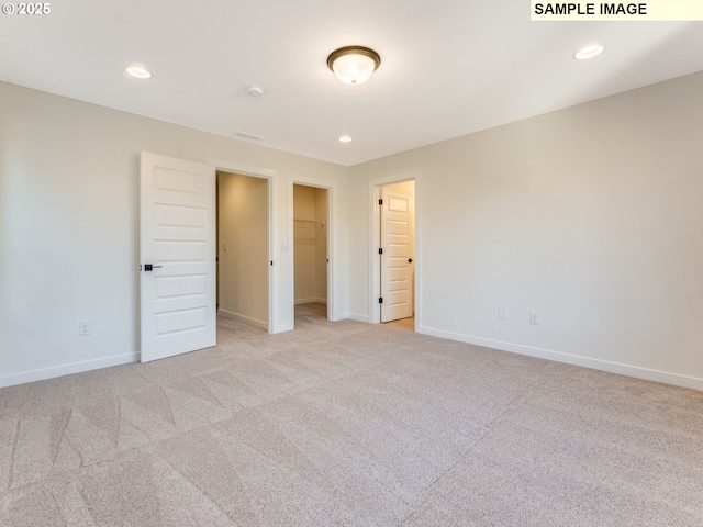 unfurnished bedroom featuring light carpet, a spacious closet, baseboards, and recessed lighting