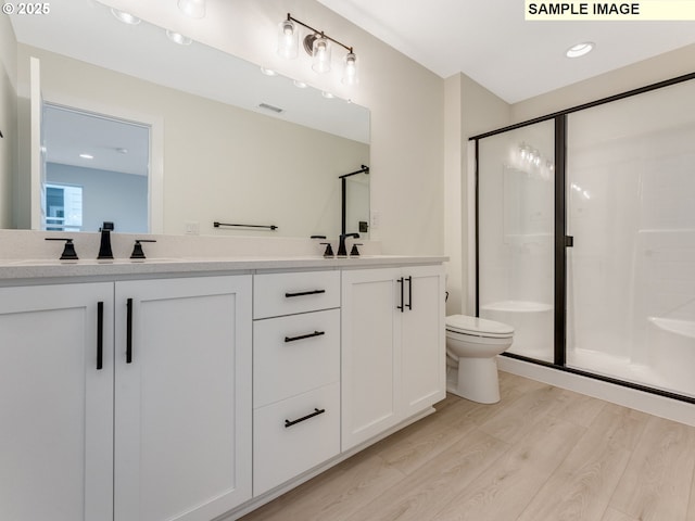 bathroom with double vanity, a shower stall, toilet, and wood finished floors