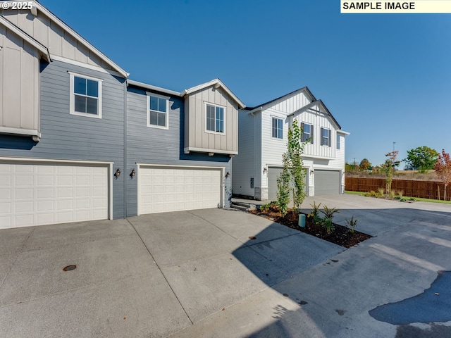 view of front facade with board and batten siding, concrete driveway, fence, and an attached garage