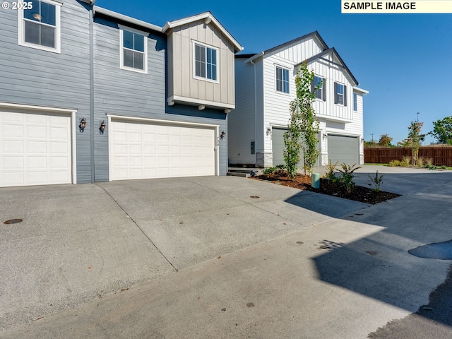 view of front of home featuring driveway, board and batten siding, an attached garage, and fence