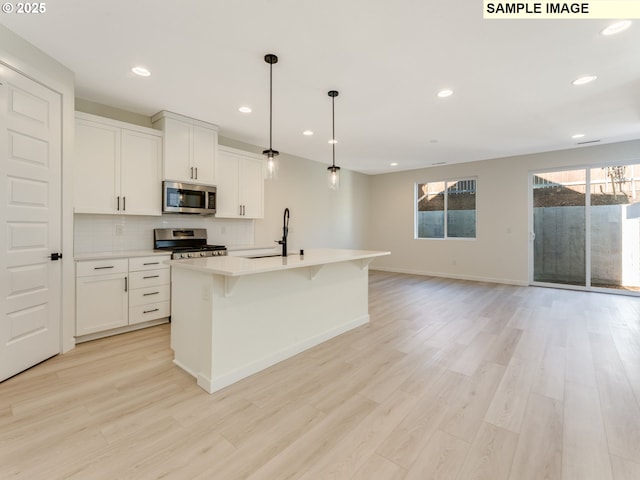 kitchen featuring light wood finished floors, light countertops, backsplash, appliances with stainless steel finishes, and a sink