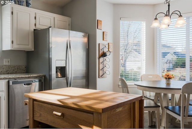 kitchen with appliances with stainless steel finishes, pendant lighting, white cabinetry, a notable chandelier, and light stone counters