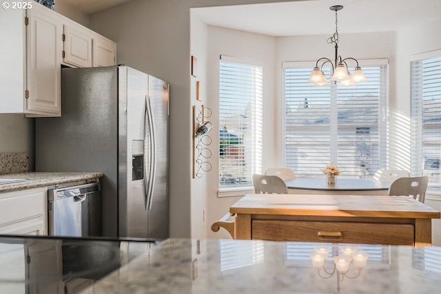 kitchen with a wealth of natural light, decorative light fixtures, white cabinetry, light stone counters, and stainless steel appliances