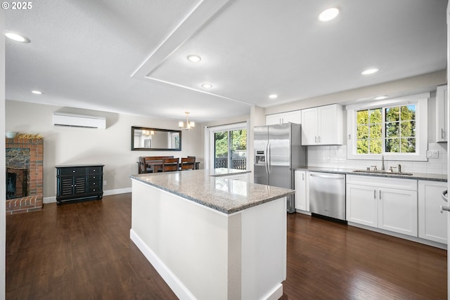 kitchen featuring an AC wall unit, white cabinetry, sink, light stone counters, and appliances with stainless steel finishes