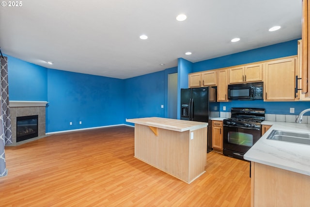 kitchen with open floor plan, a fireplace, light wood-style floors, black appliances, and a sink