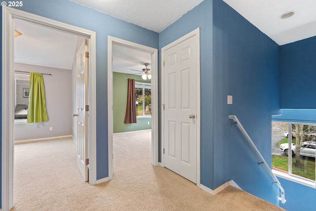 hallway featuring carpet flooring, an upstairs landing, and baseboards