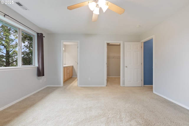 unfurnished bedroom featuring a walk in closet, baseboards, visible vents, and light carpet