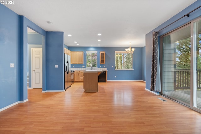 kitchen featuring light wood finished floors, a center island, light countertops, a notable chandelier, and stainless steel fridge