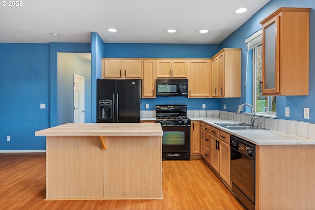 kitchen with a kitchen island, light countertops, light wood-style flooring, black appliances, and a sink