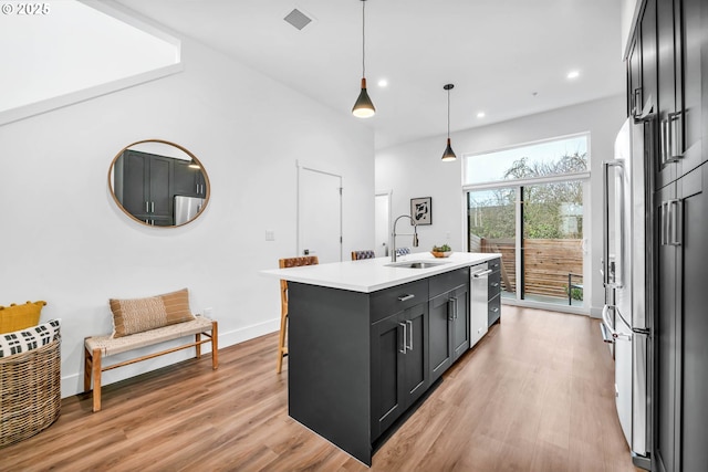 kitchen with pendant lighting, a kitchen island with sink, sink, light wood-type flooring, and appliances with stainless steel finishes