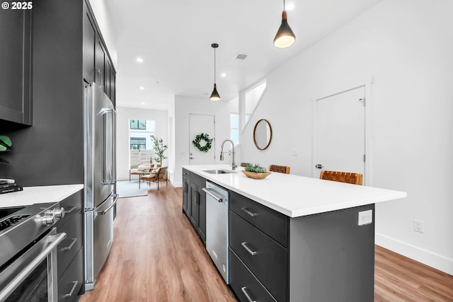 kitchen featuring pendant lighting, a kitchen island with sink, sink, light hardwood / wood-style floors, and stainless steel appliances