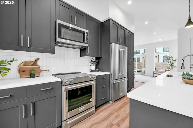 kitchen featuring sink, stainless steel appliances, backsplash, pendant lighting, and light wood-type flooring