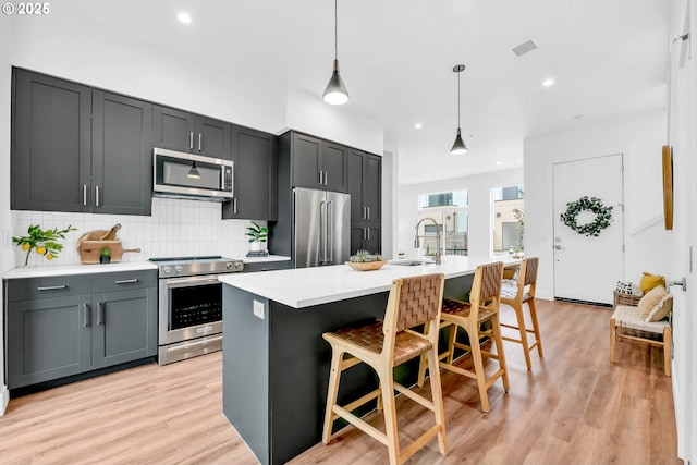 kitchen with a kitchen island with sink, sink, hanging light fixtures, appliances with stainless steel finishes, and a breakfast bar area