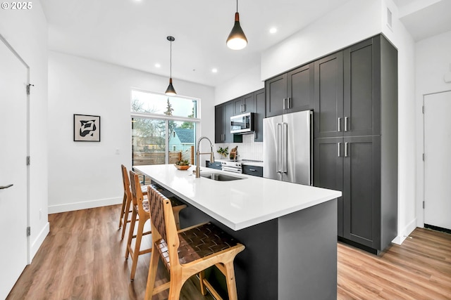 kitchen featuring sink, hanging light fixtures, stainless steel appliances, a breakfast bar area, and a kitchen island with sink