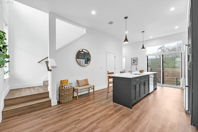 kitchen with a kitchen bar, appliances with stainless steel finishes, pendant lighting, a center island with sink, and light hardwood / wood-style flooring