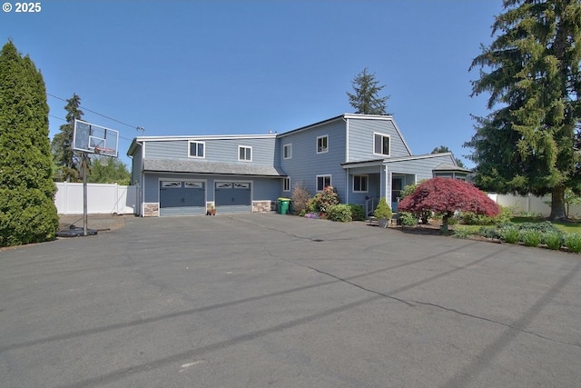 view of front of house with an attached garage, fence, driveway, and stone siding