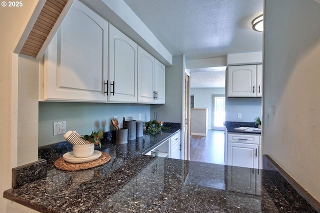 kitchen with dark stone counters, baseboards, a textured ceiling, and white cabinetry