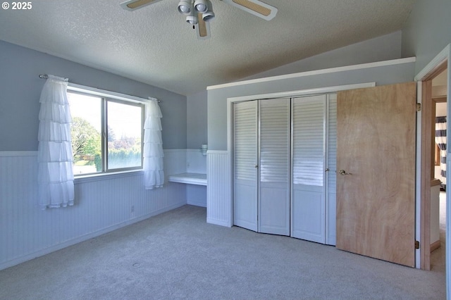unfurnished bedroom featuring ceiling fan, wainscoting, a textured ceiling, carpet, and a closet